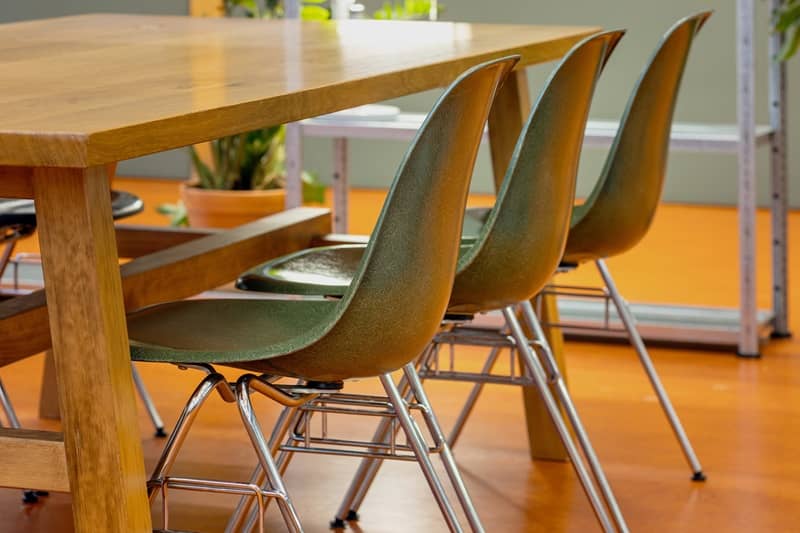 Detailaufnahme von drei gr&uuml;nen Fiberglassst&uuml;hlen, die an einem Holztisch stehen